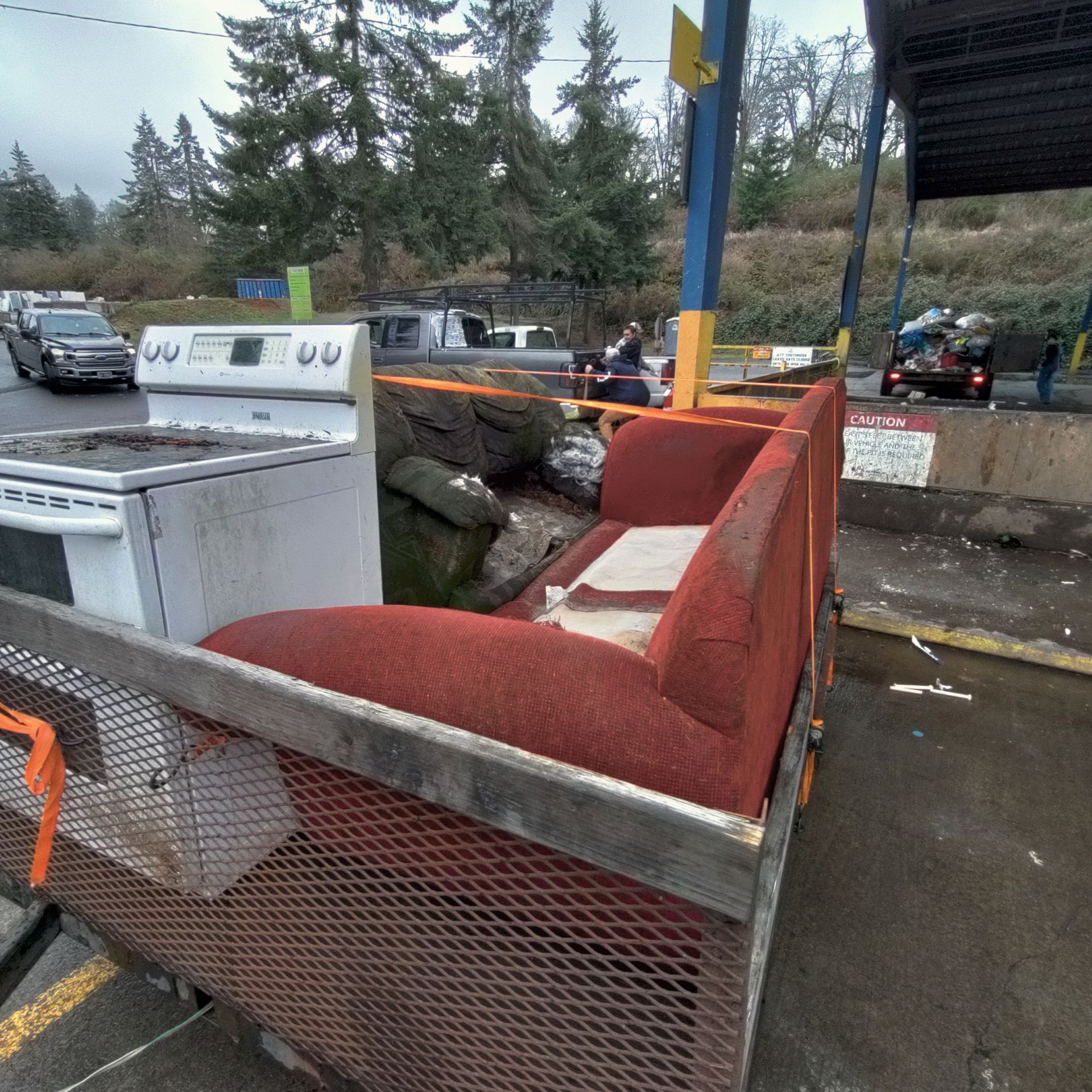 A pickup truck bed overflowing with discarded furniture and appliances at a waste disposal site.