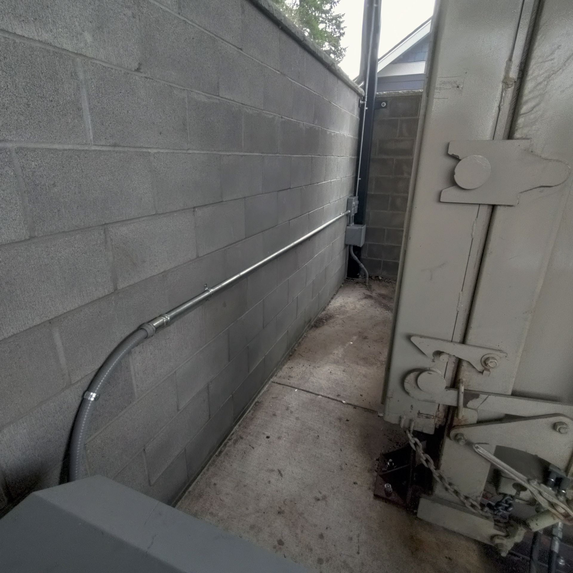 Gray cinder block wall with electrical conduit and a large metal door on the right.