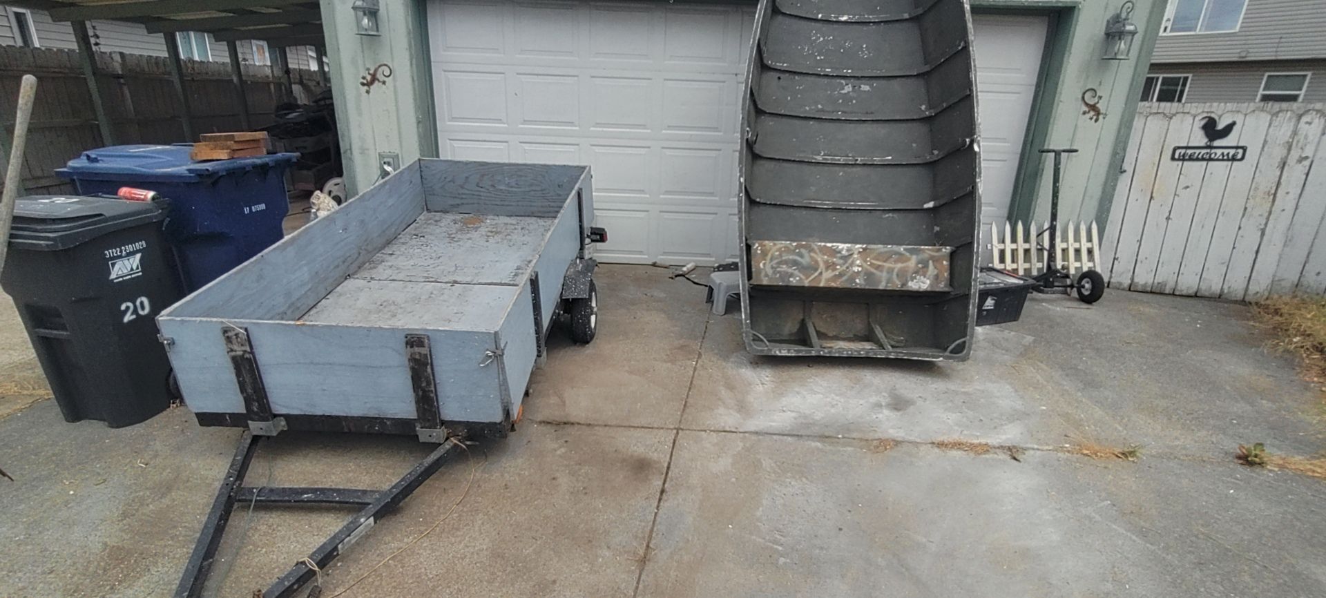 A trailer and a large, black, industrial-looking machine sit in front of a garage.