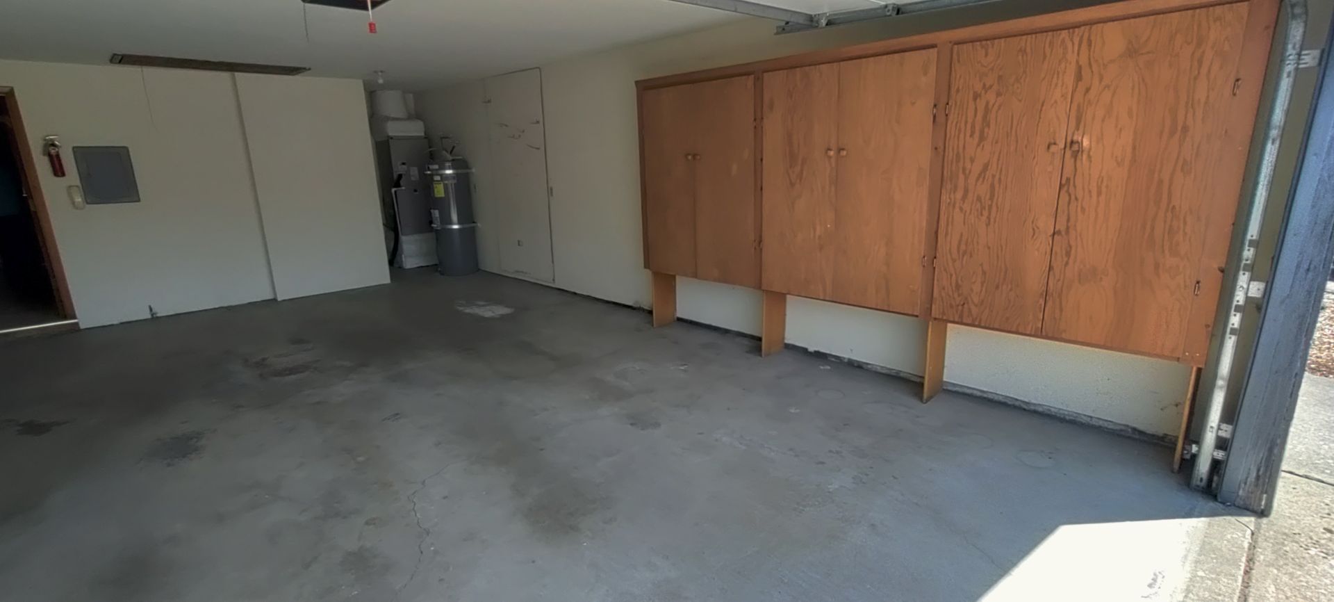 Interior of a garage with concrete floor and wooden storage cabinets. The garage door is open.