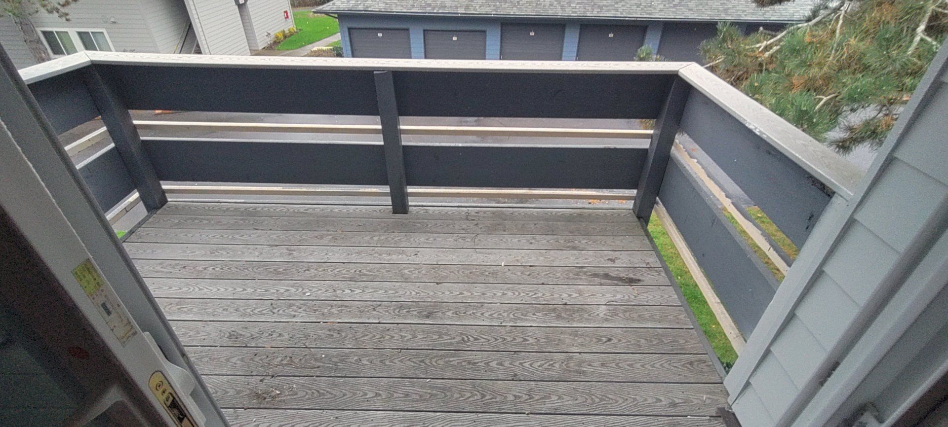 Overhead view of a deck with gray roofing material, surrounded by black railings and a yard in the distance.