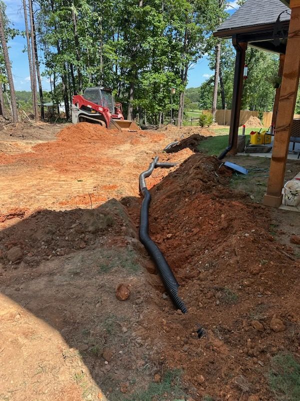 A drain pipe is being installed in the dirt in front of a house.
