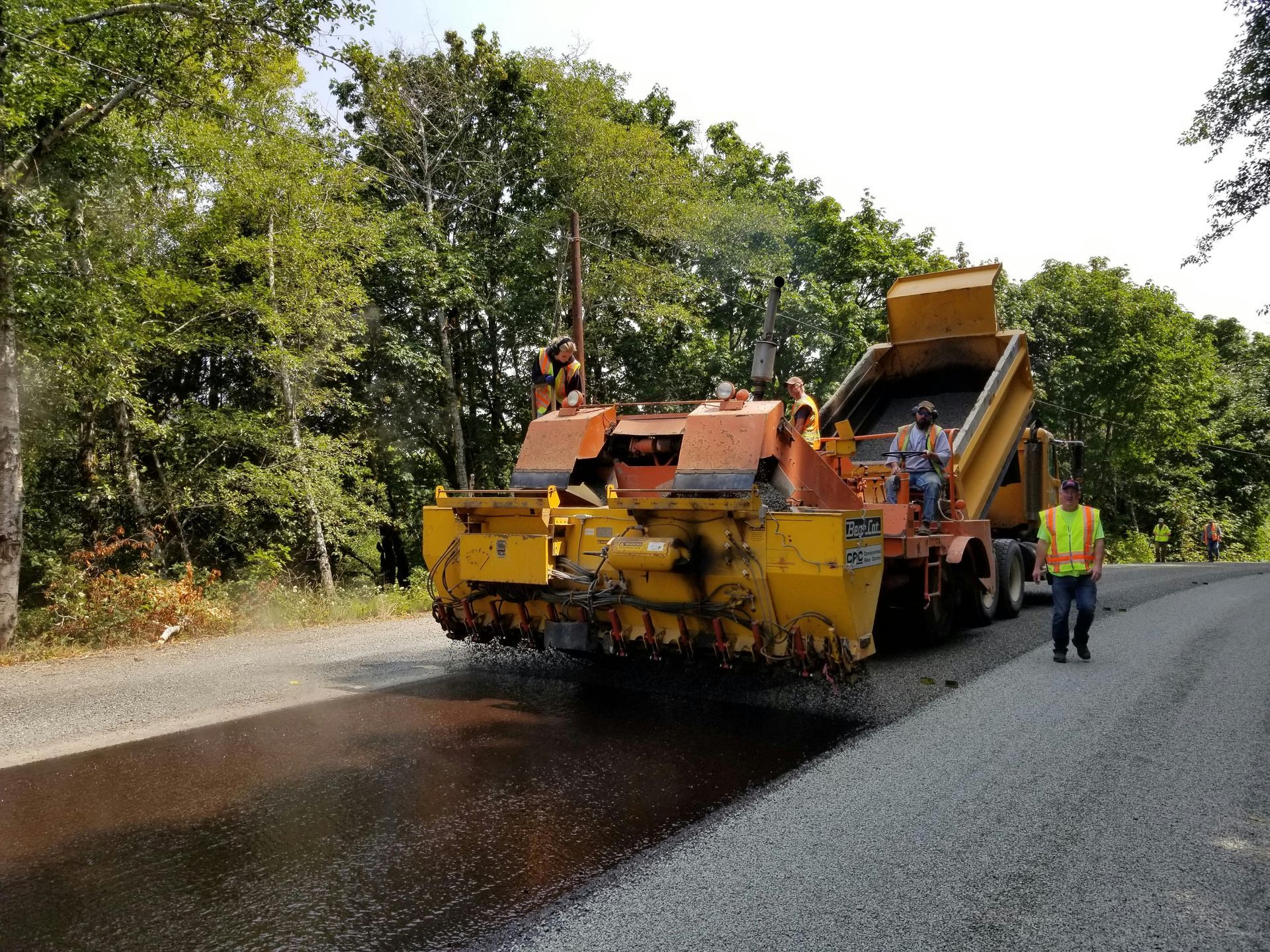 A man is walking down a road next to a machine that is laying asphalt.