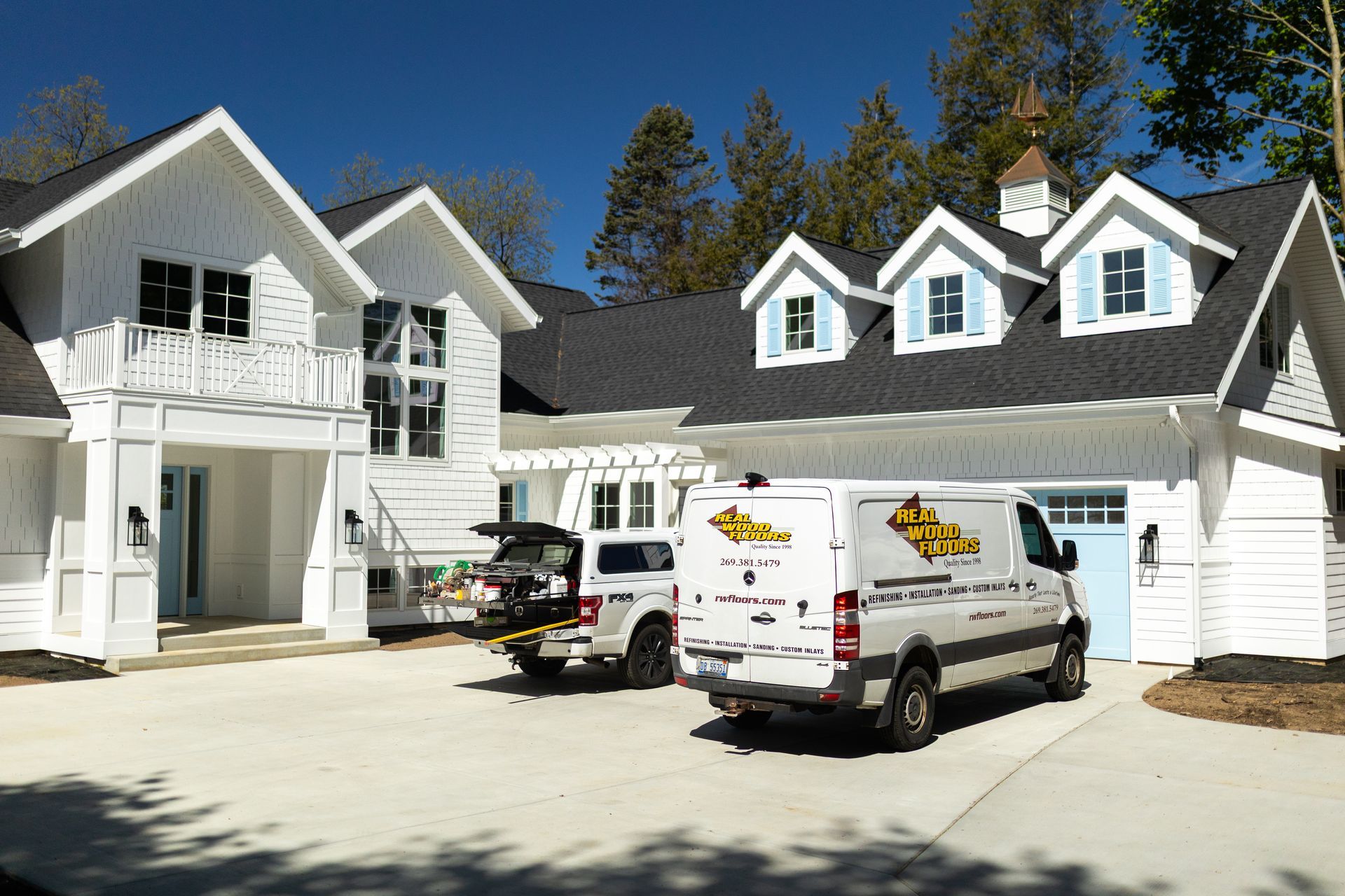 Two white vans are parked in front of a large white house
