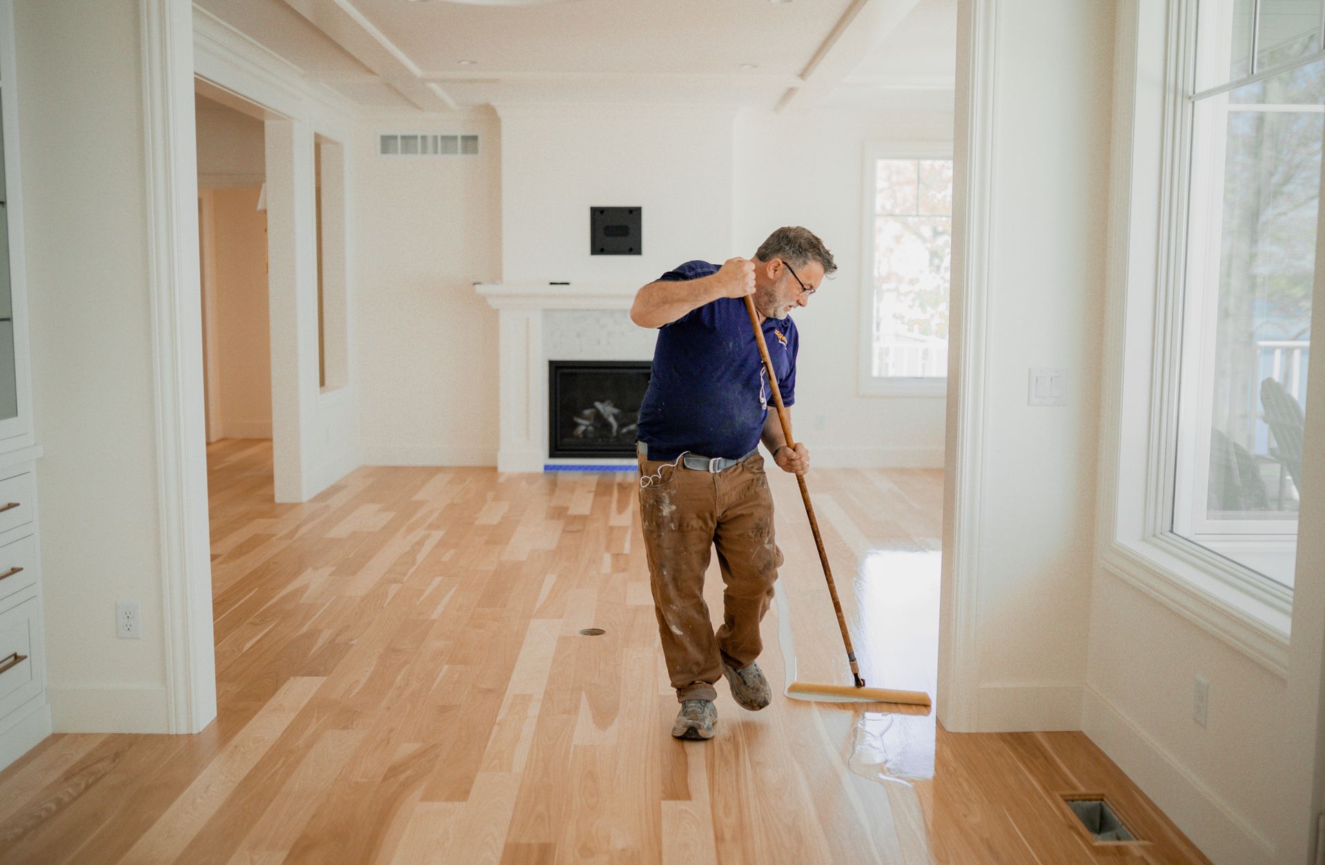 A man is cleaning a wooden floor with a broom in an empty room.