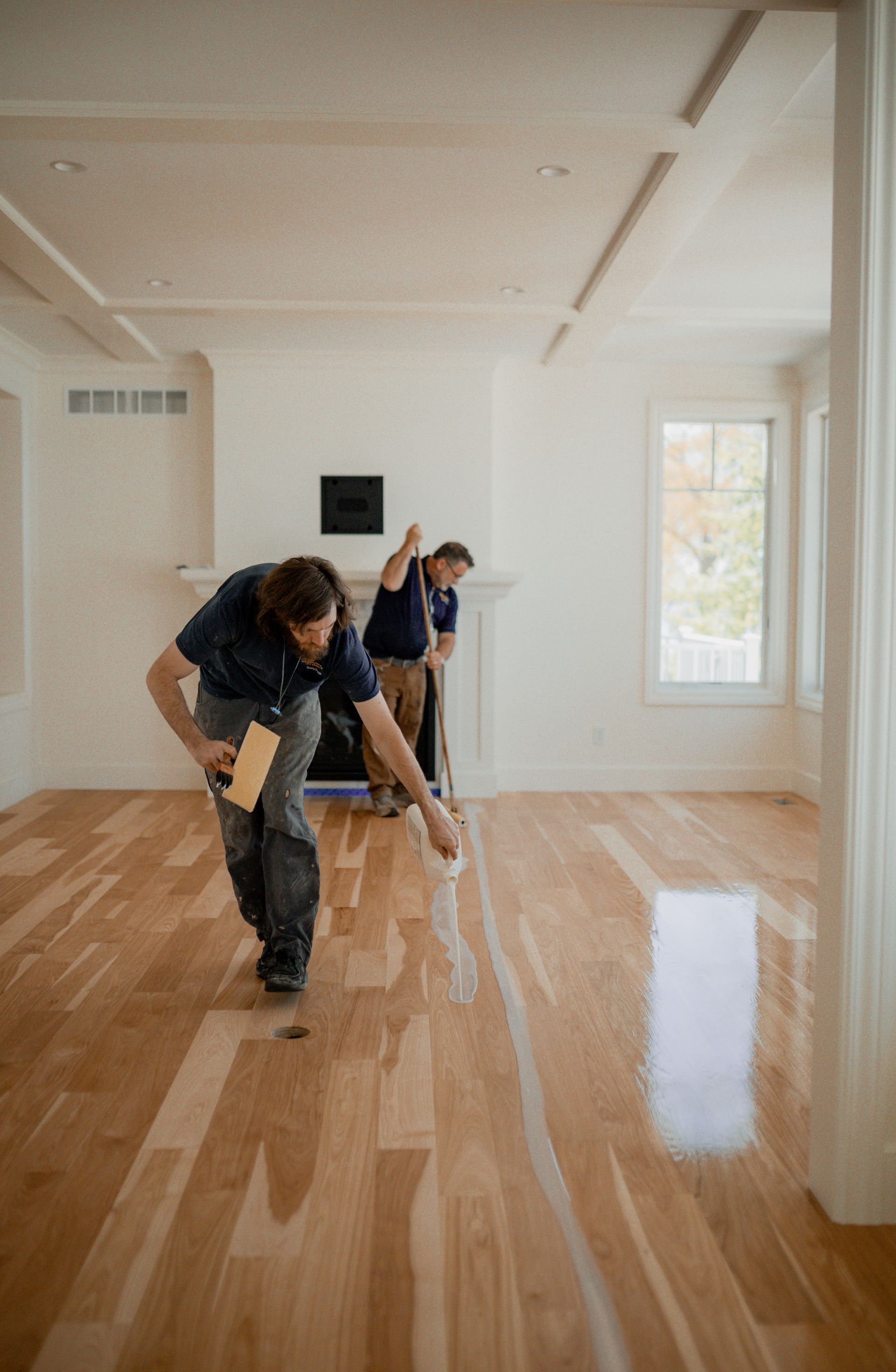 Flooring specialists are applying finish a wooden floor in a living room.