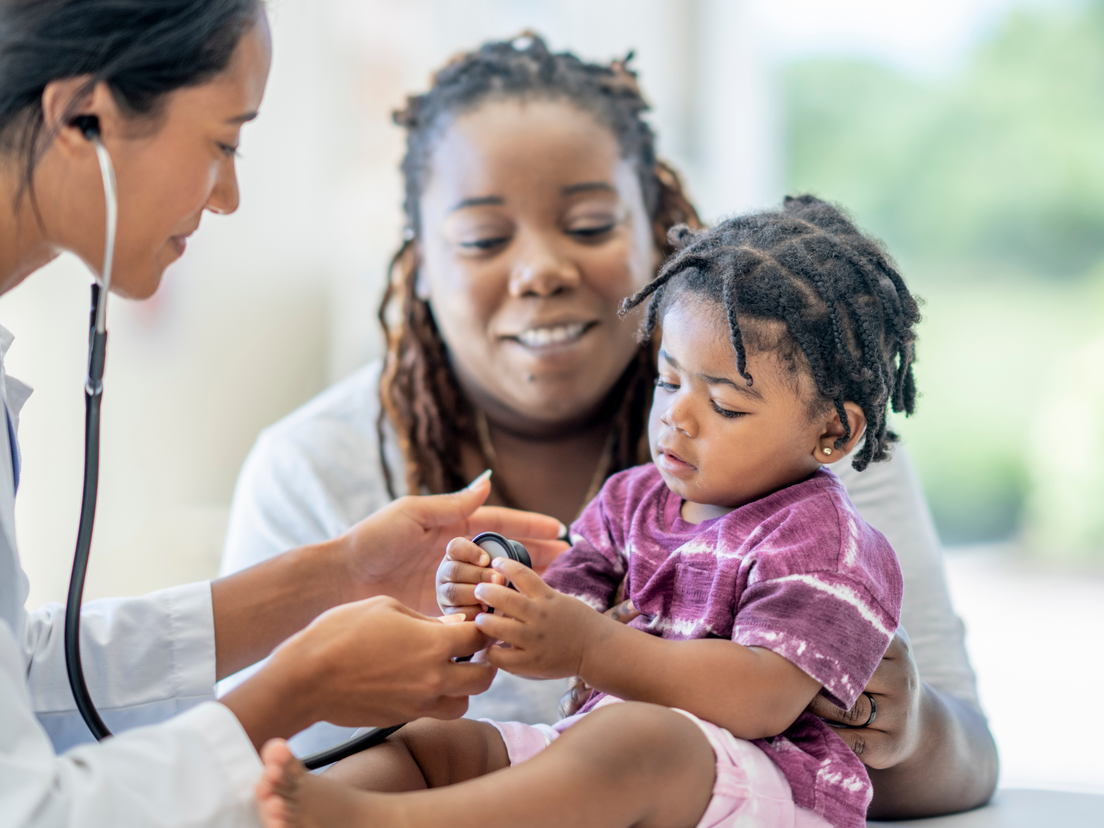 A mother is holding a child while a pediatrician examines the child