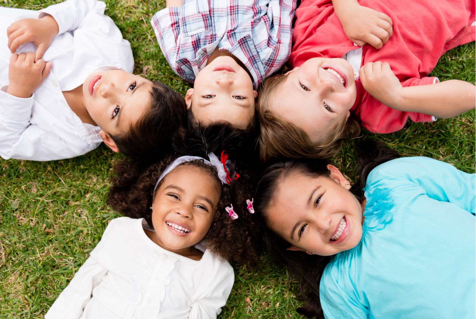 A group of children are lying in the grass smiling and laughing