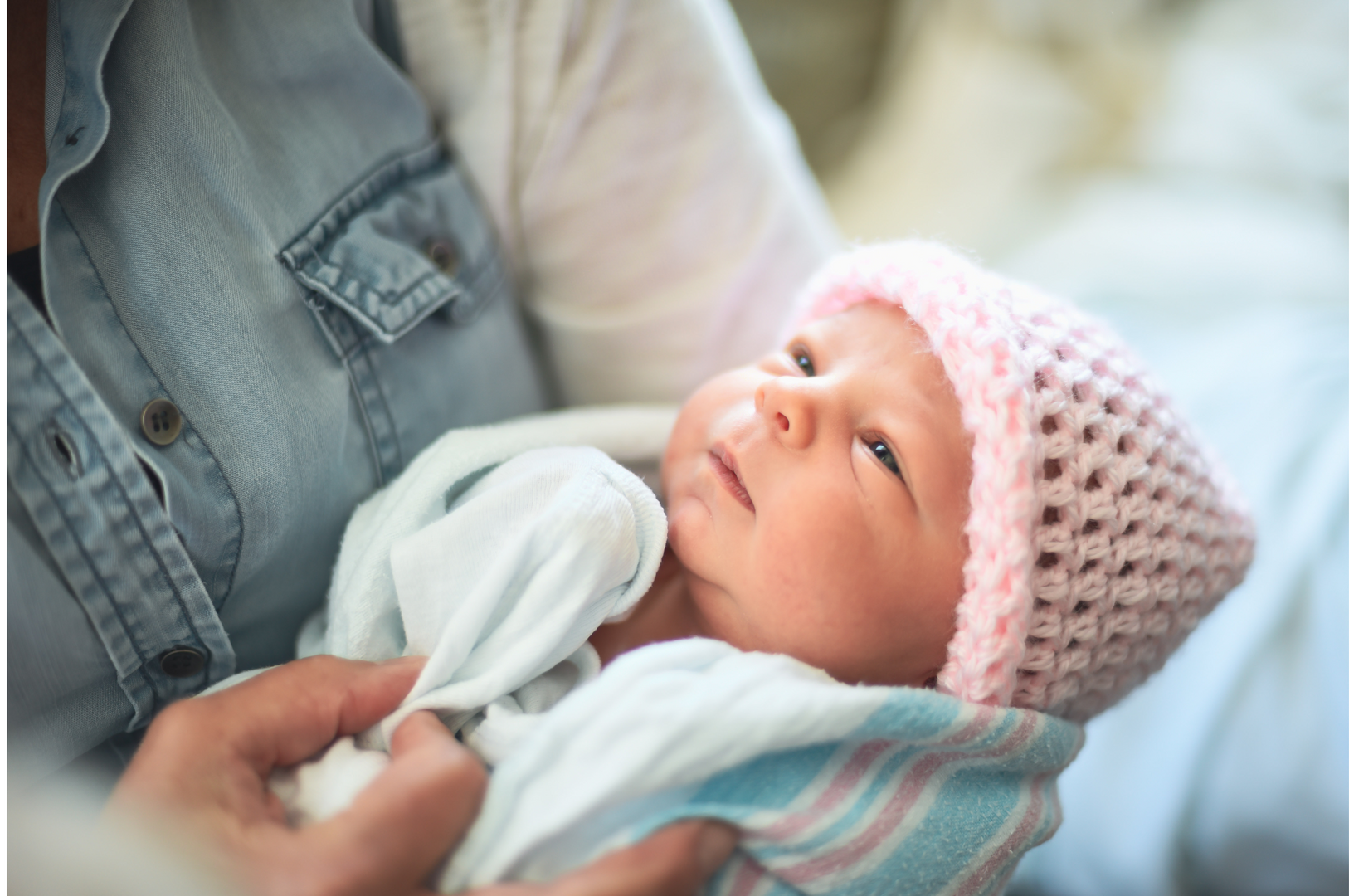 A parent is holding a newborn baby in a blanket and hat