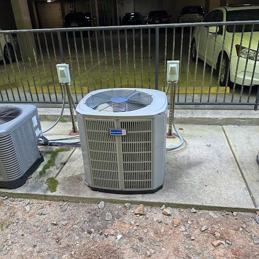 Two air conditioners are sitting on a sidewalk next to a fence.