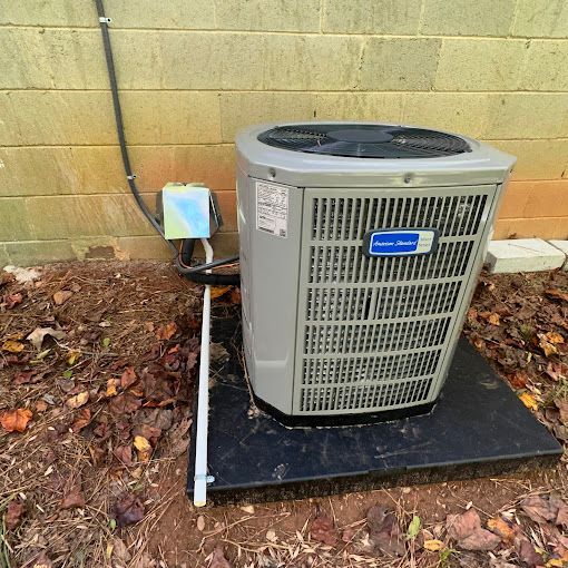 A large air conditioner is sitting on top of a black mat in front of a brick wall.