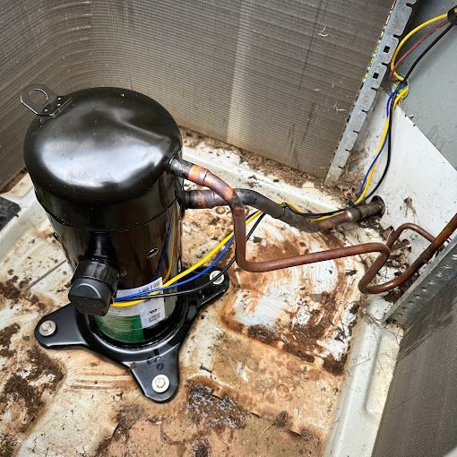 A black compressor is sitting on the floor next to a copper pipe.