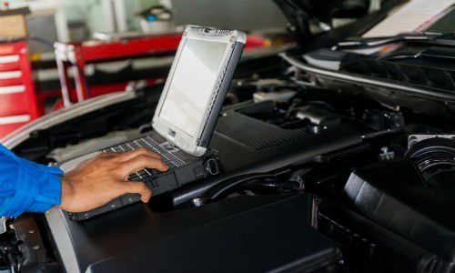 una mano che usa un computer portatile appoggiato sul motore di una macchina