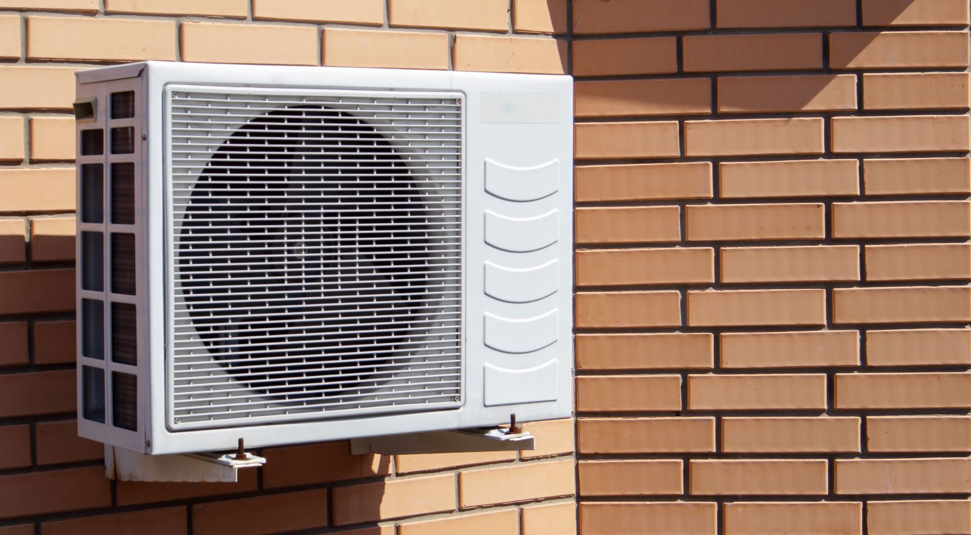 White air conditioning unit mounted on a brick wall, casting a shadow.
