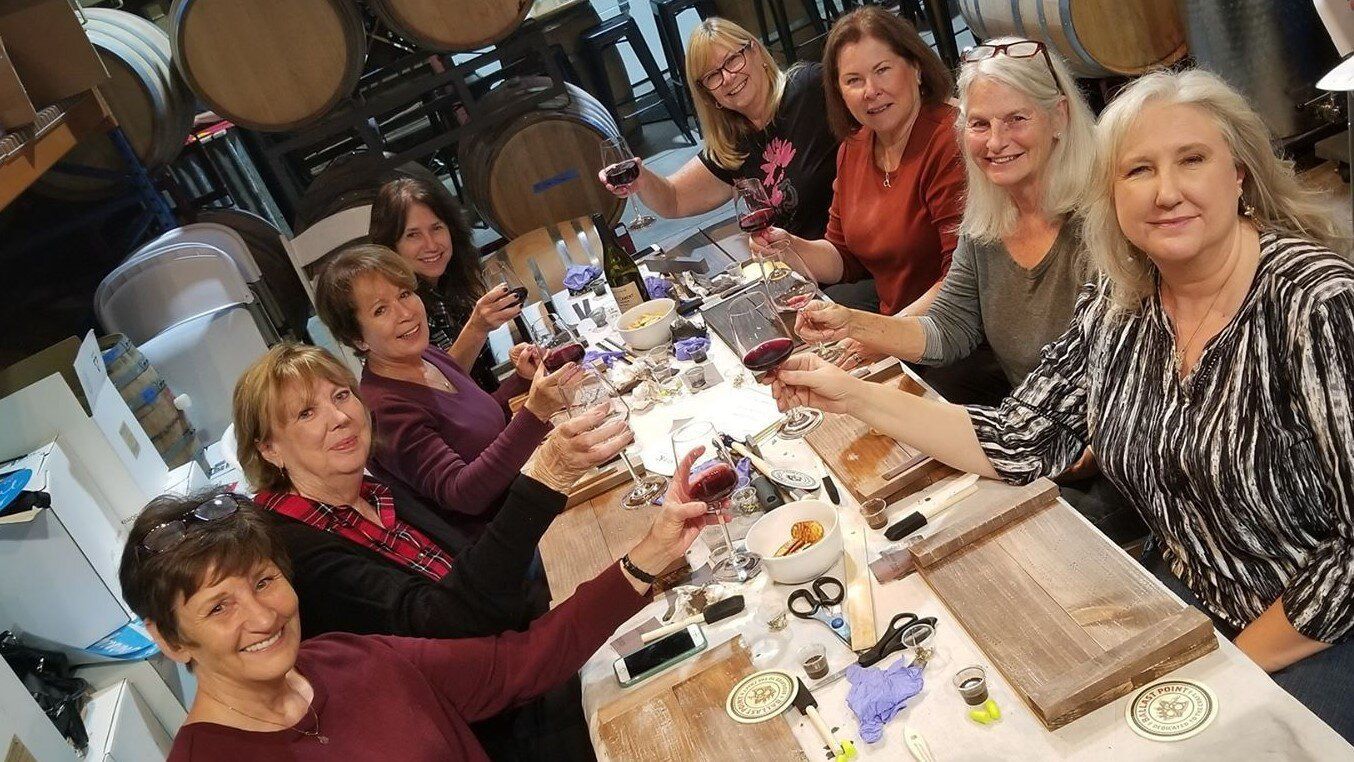 A group of women are sitting around a table toasting with wine glasses.