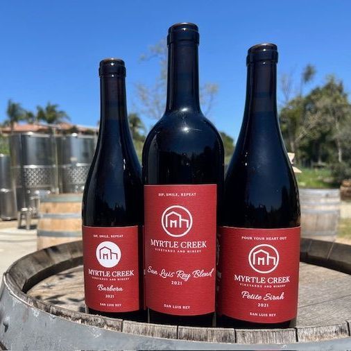 Three bottles of wine are sitting on top of a wooden barrel.