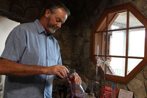 A man is pouring liquid into a bottle in front of a window.