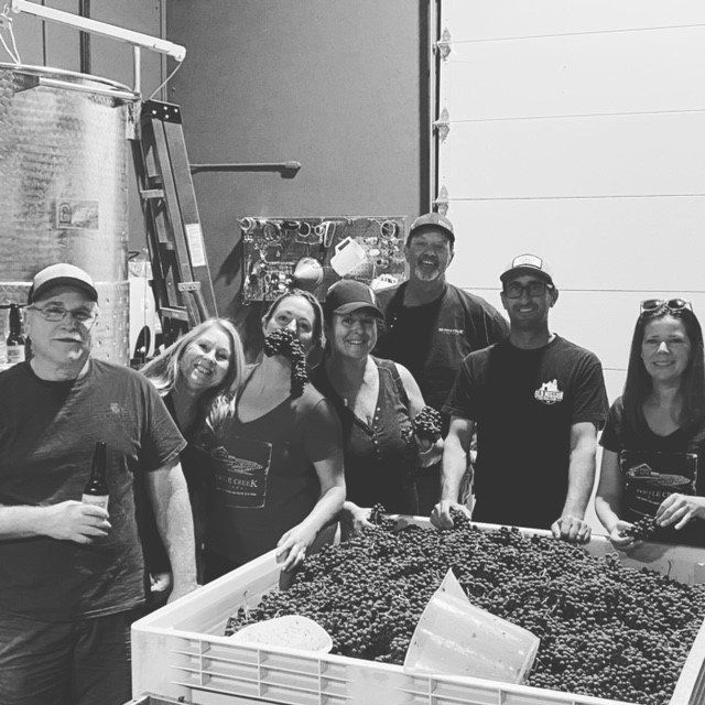 A group of people standing around a crate of grapes