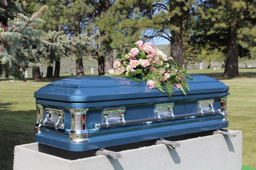 A blue coffin with pink roses on top of it is sitting on top of a concrete block in a cemetery.