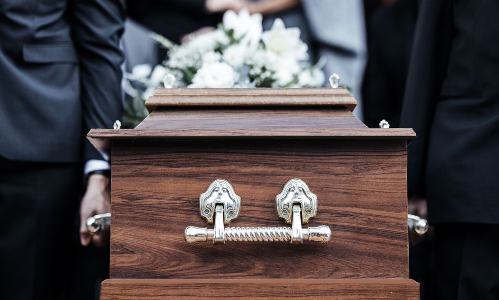 A group of people are carrying a wooden coffin at a funeral.