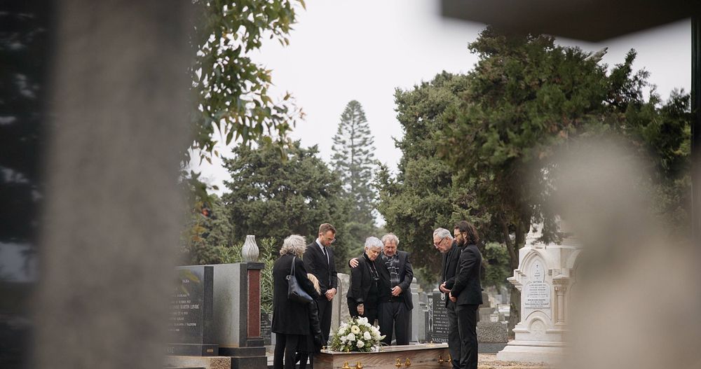 A group of people are standing around a grave in a cemetery.