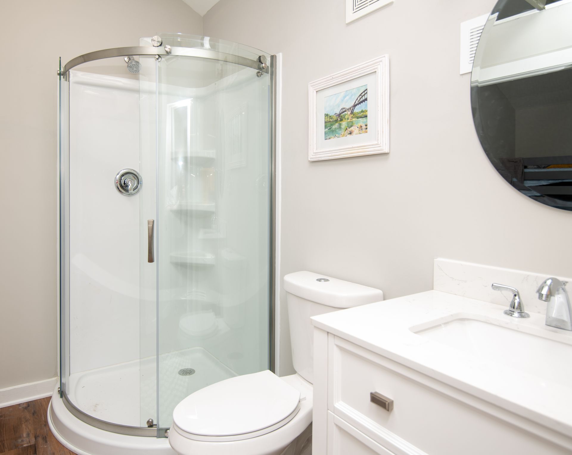 Bathroom with white shower, toilet, vanity, and round mirror; gray walls.