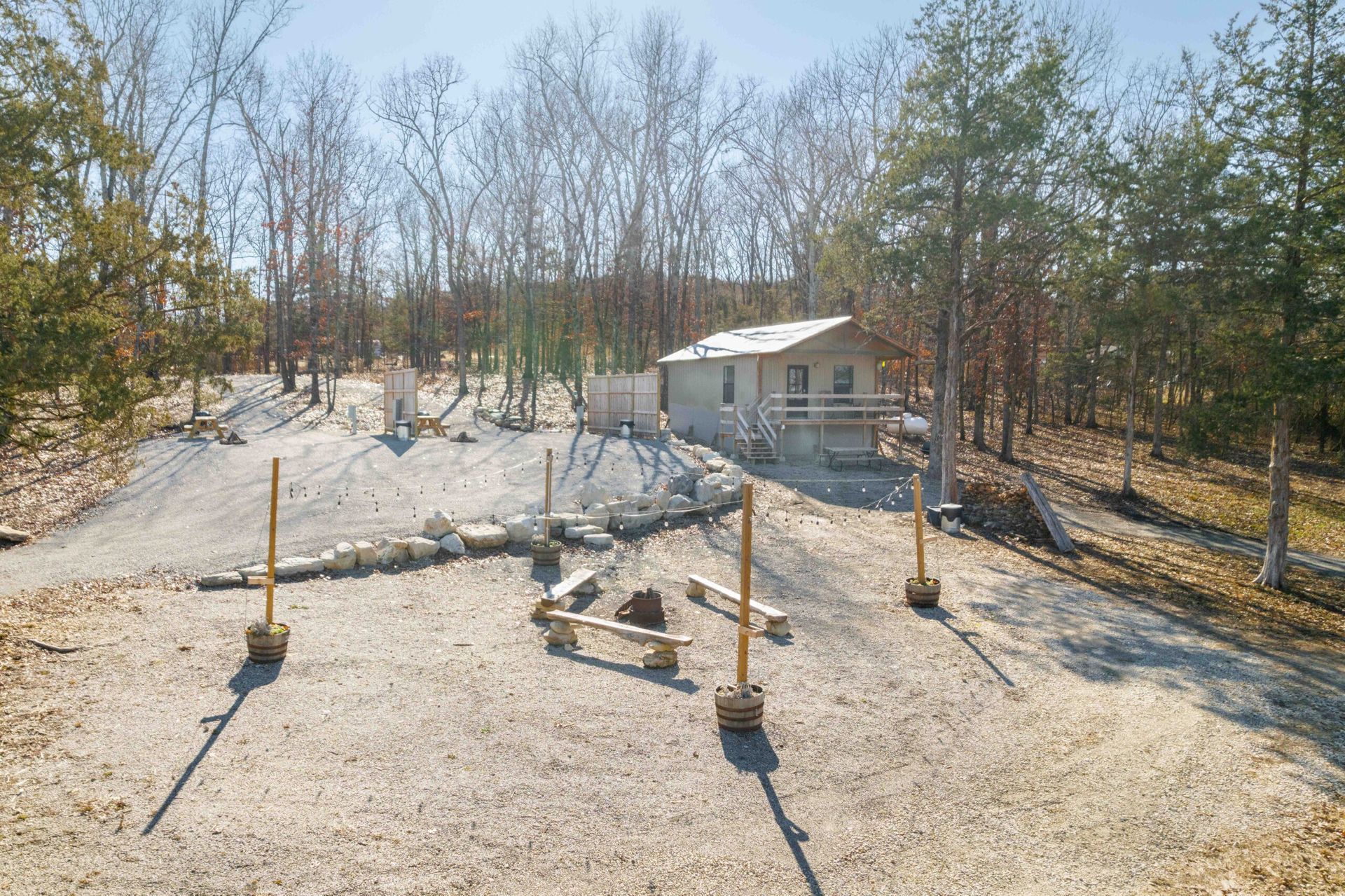 Small cabin with gravel yard, fire pit, and wooden benches in a wooded area.