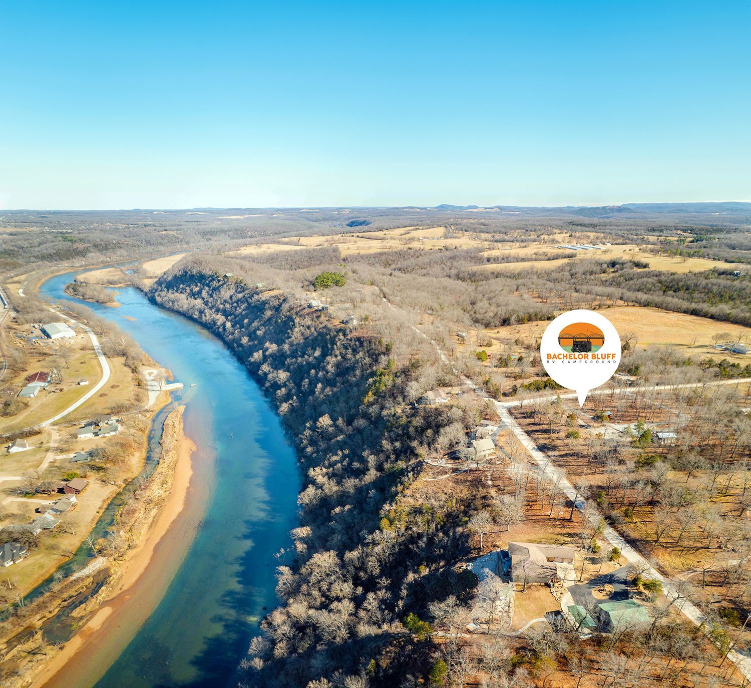 Aerial view: river next to treeline, fields, and a road. Sign for 