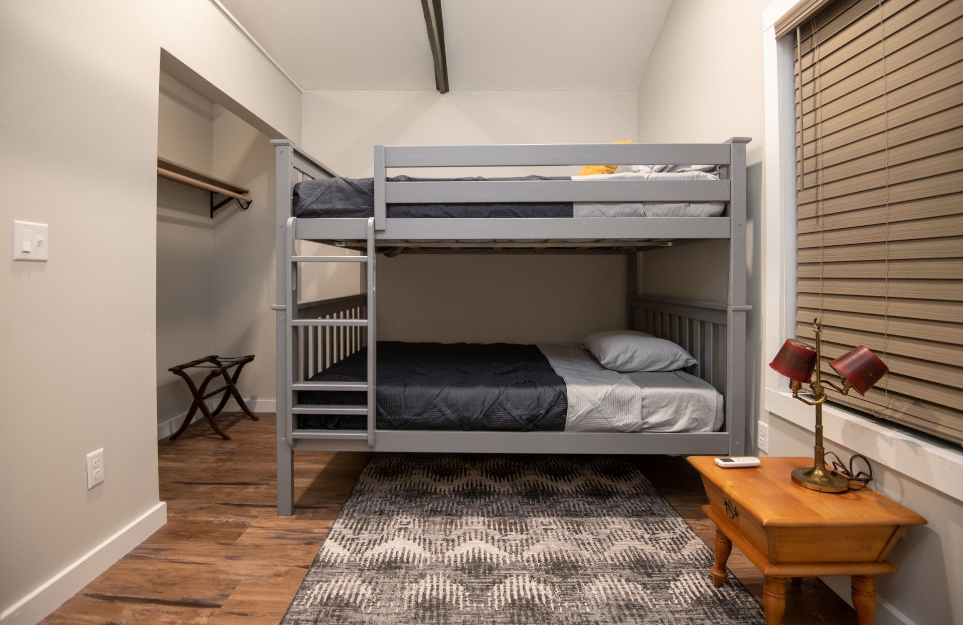 Bunk beds in a room with a rug, bedside table, and closet. Brown hardwood floors and beige walls.