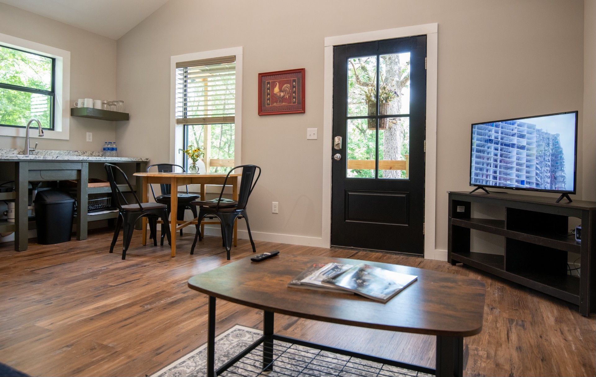 Cozy living space with kitchen, dining table, and TV. Wooden floors, gray walls, and black door.