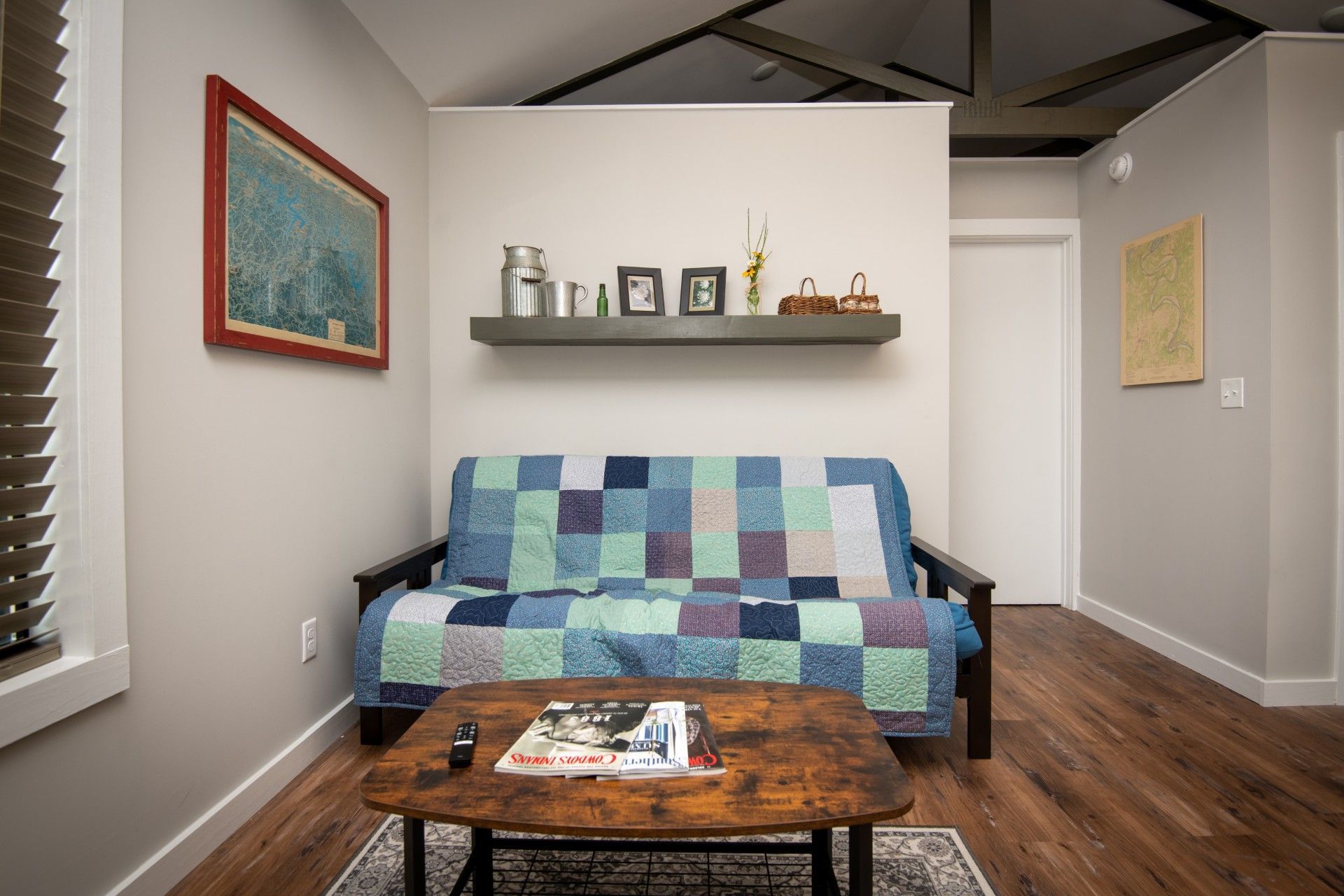 Living room with a futon, coffee table, shelf, artwork, and hardwood floors.