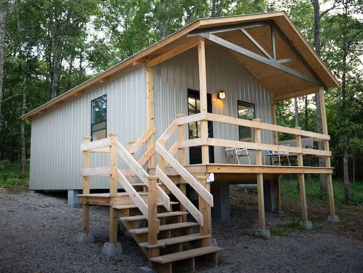 Cabin with a porch and wooden stairs, set amongst trees.