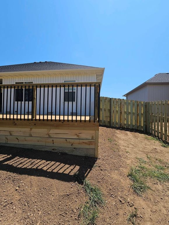Small white house with a metal carport, fenced yard, and gravel under a bright blue sky