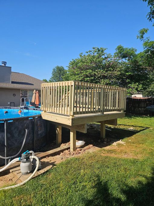 Small wooden deck platform beside an above-ground pool in a sunny backyard