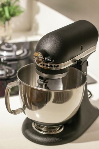 Black KitchenAid stand mixer with stainless steel bowl, on a white countertop.