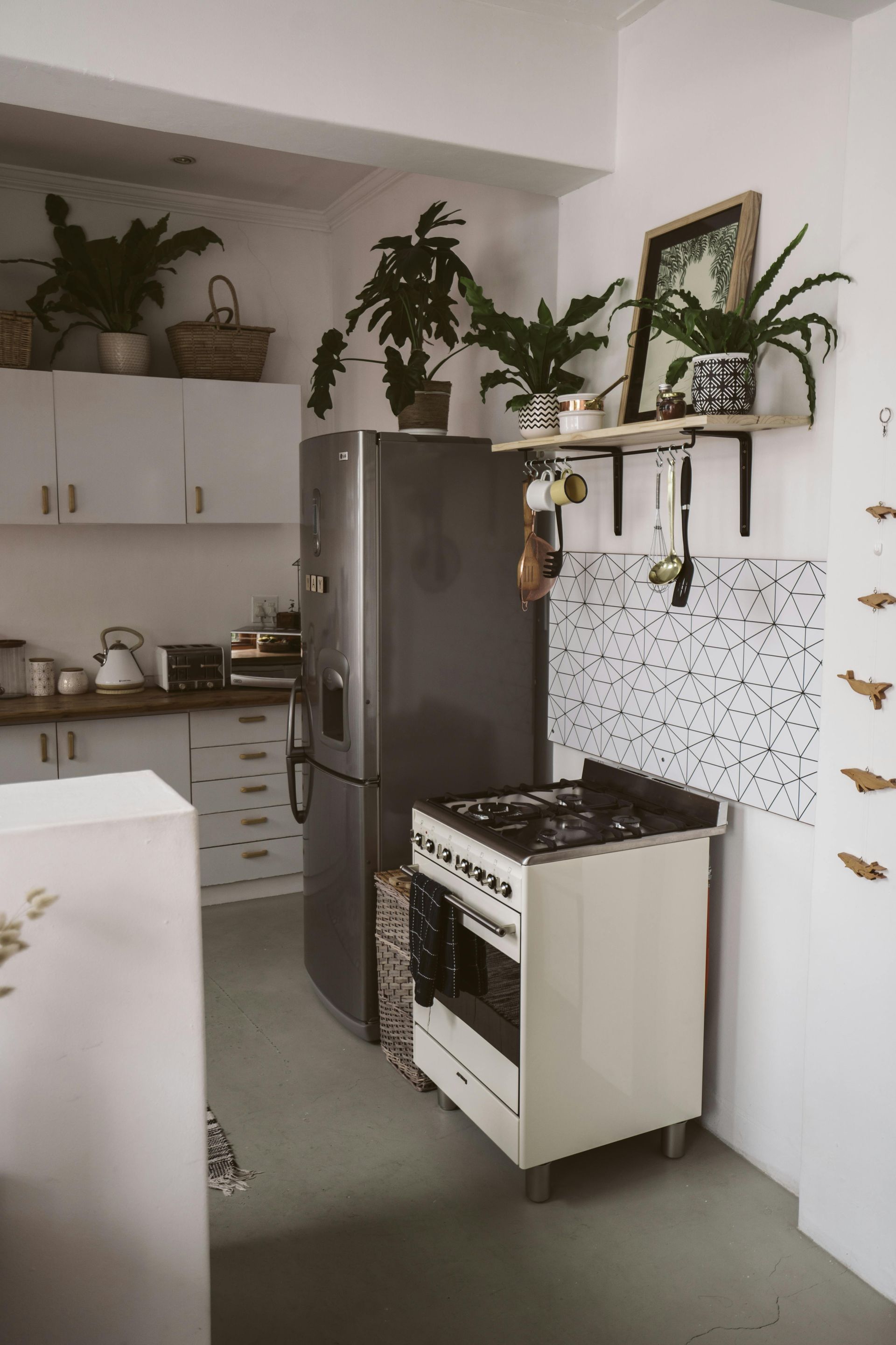 Cozy kitchen with plants, white cabinets, appliances, and gray floor.