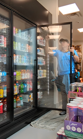 Person opening a glass freezer door in a convenience store aisle with drinks on shelves nearby