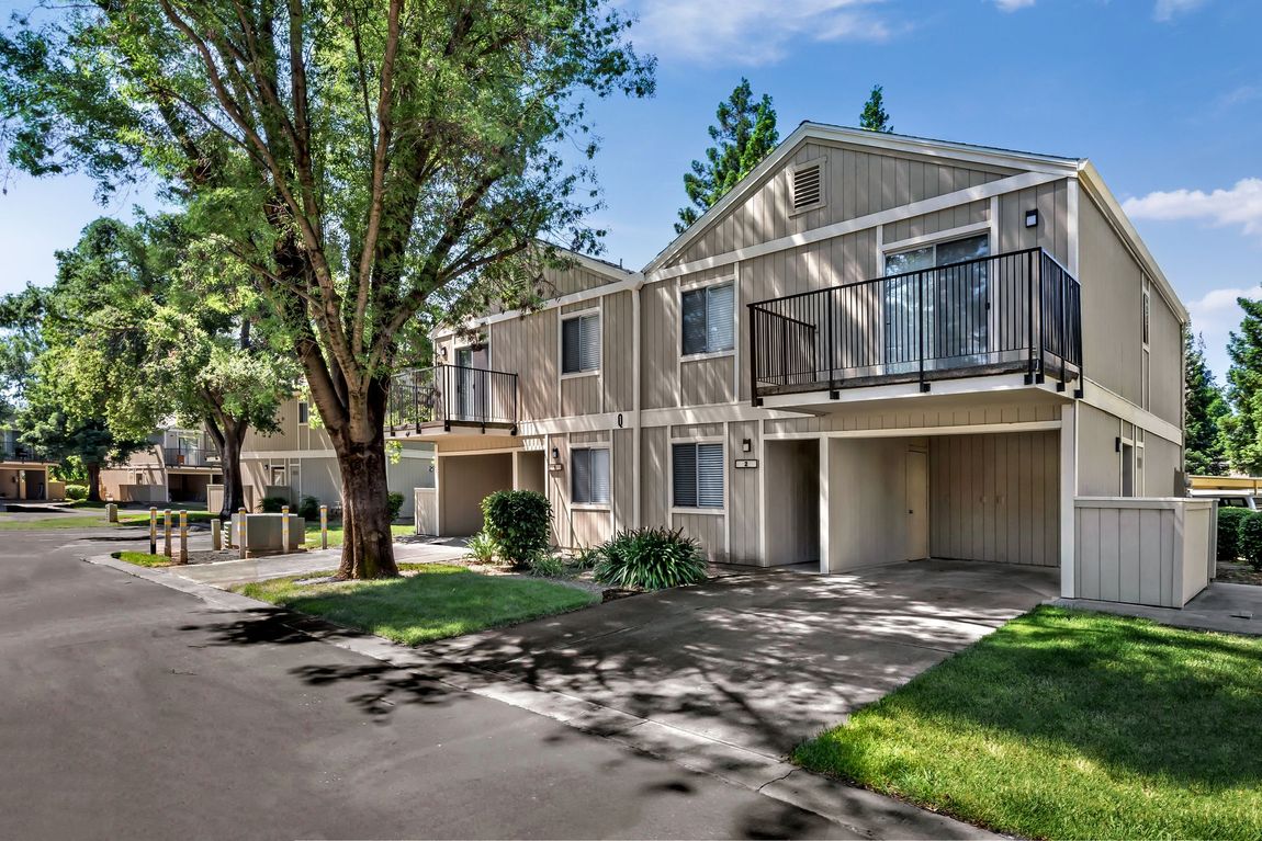 Townhouse complex with beige siding, balconies, and a tree-lined street.