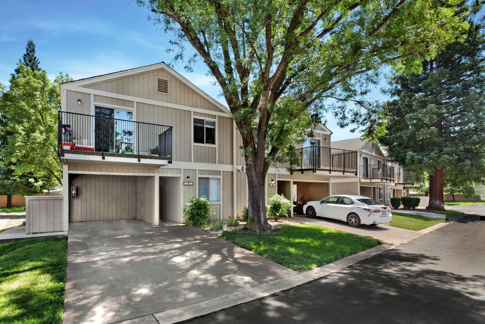 Row of beige townhouses with balconies and attached garages; car parked in driveway.
