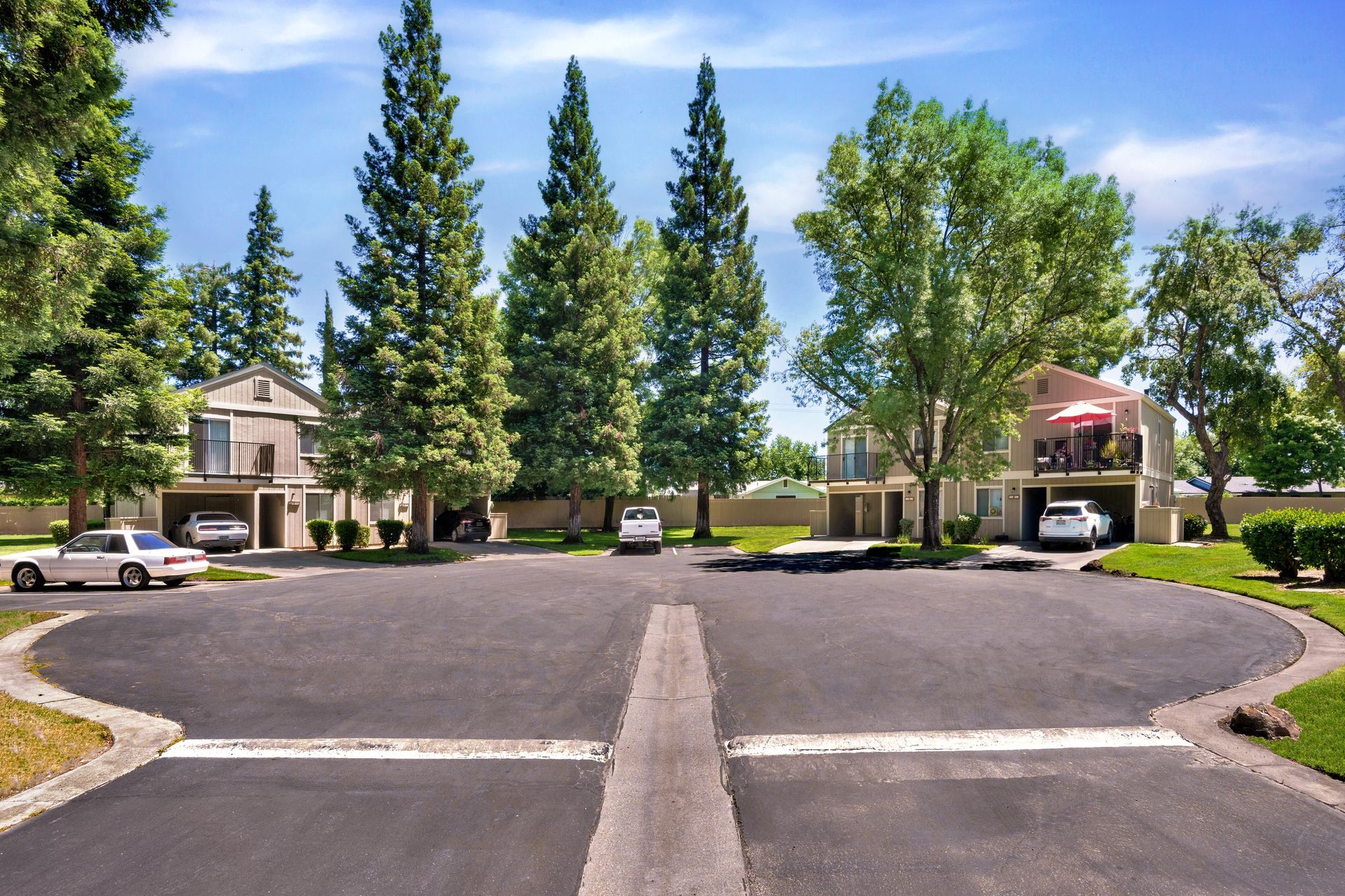 Apartment building with covered parking; cars parked under a metal canopy on a sunny day.
