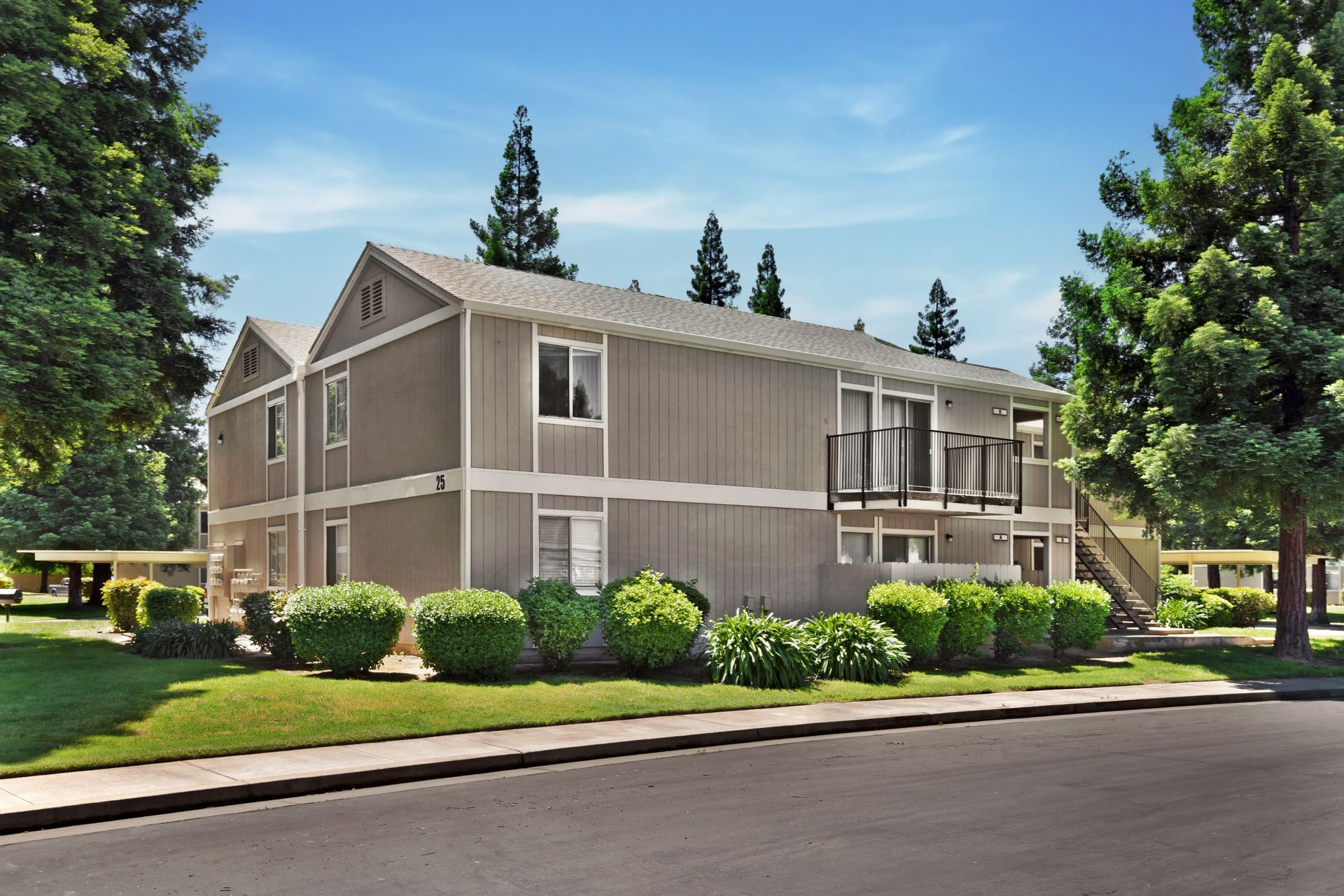Two-story beige apartment building with green landscaping and blue sky.