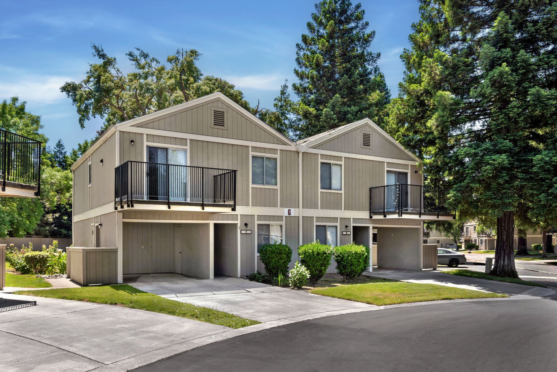 Two-story tan townhouses with black balconies, driveways, and trees in the background.