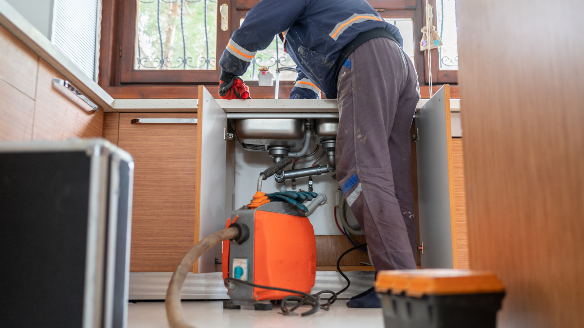 A man is cleaning a kitchen sink with a vacuum cleaner.