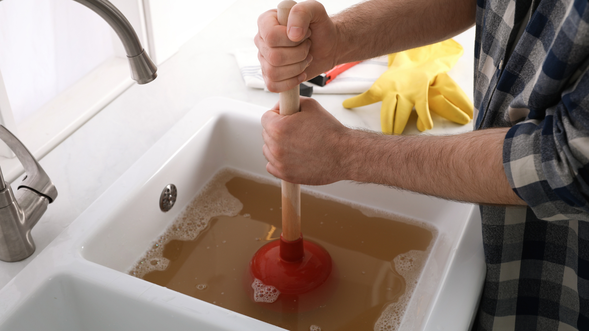 A man is using a plunger to unblock a sink.