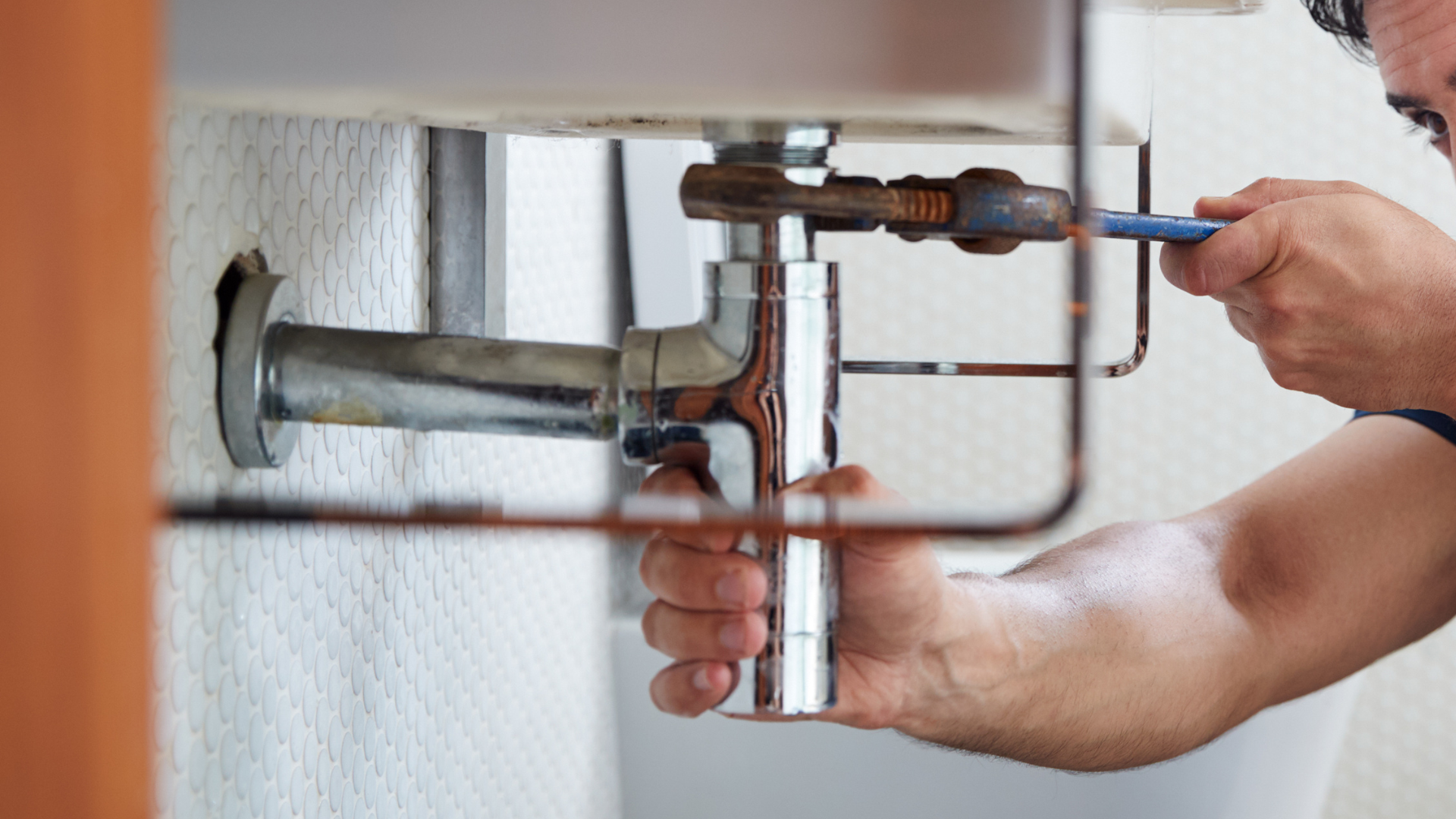 A man is fixing a sink with a screwdriver.