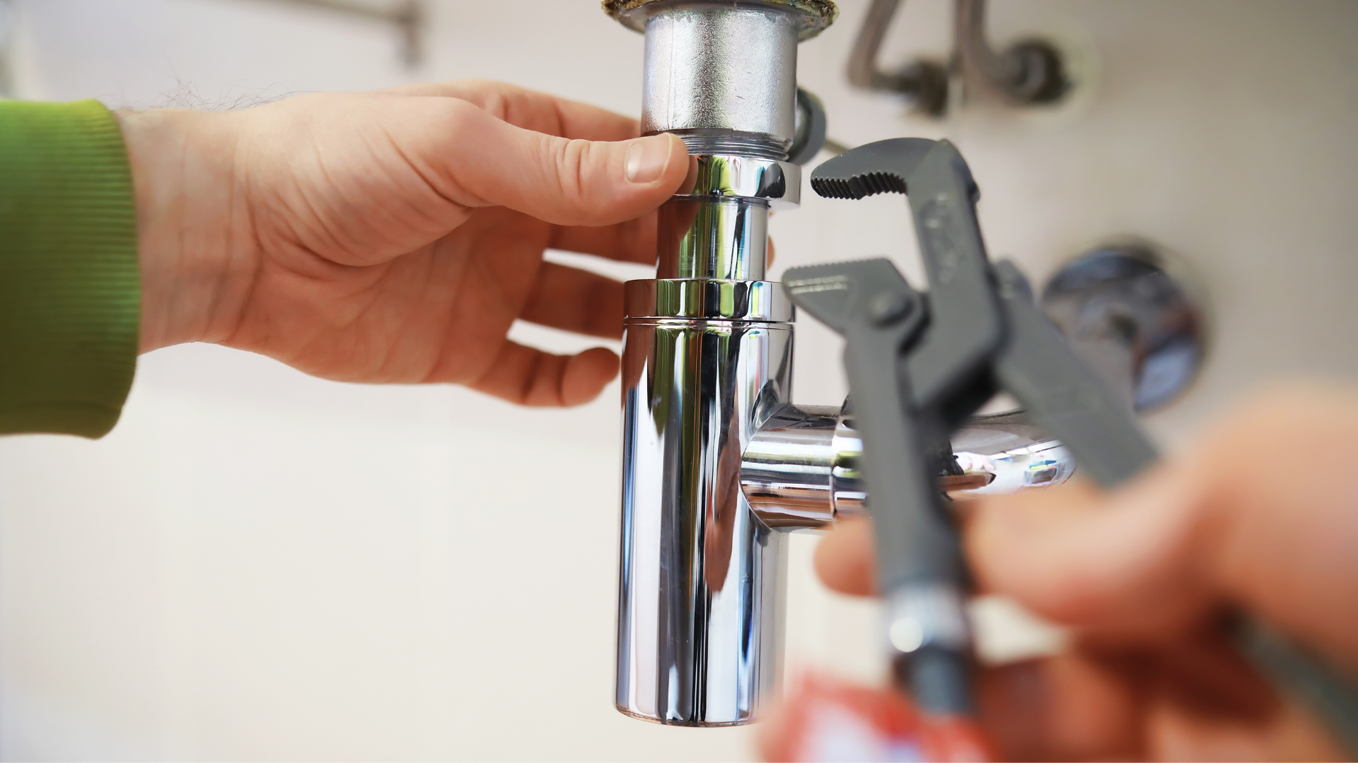 A person is fixing a sink pipe with a wrench.