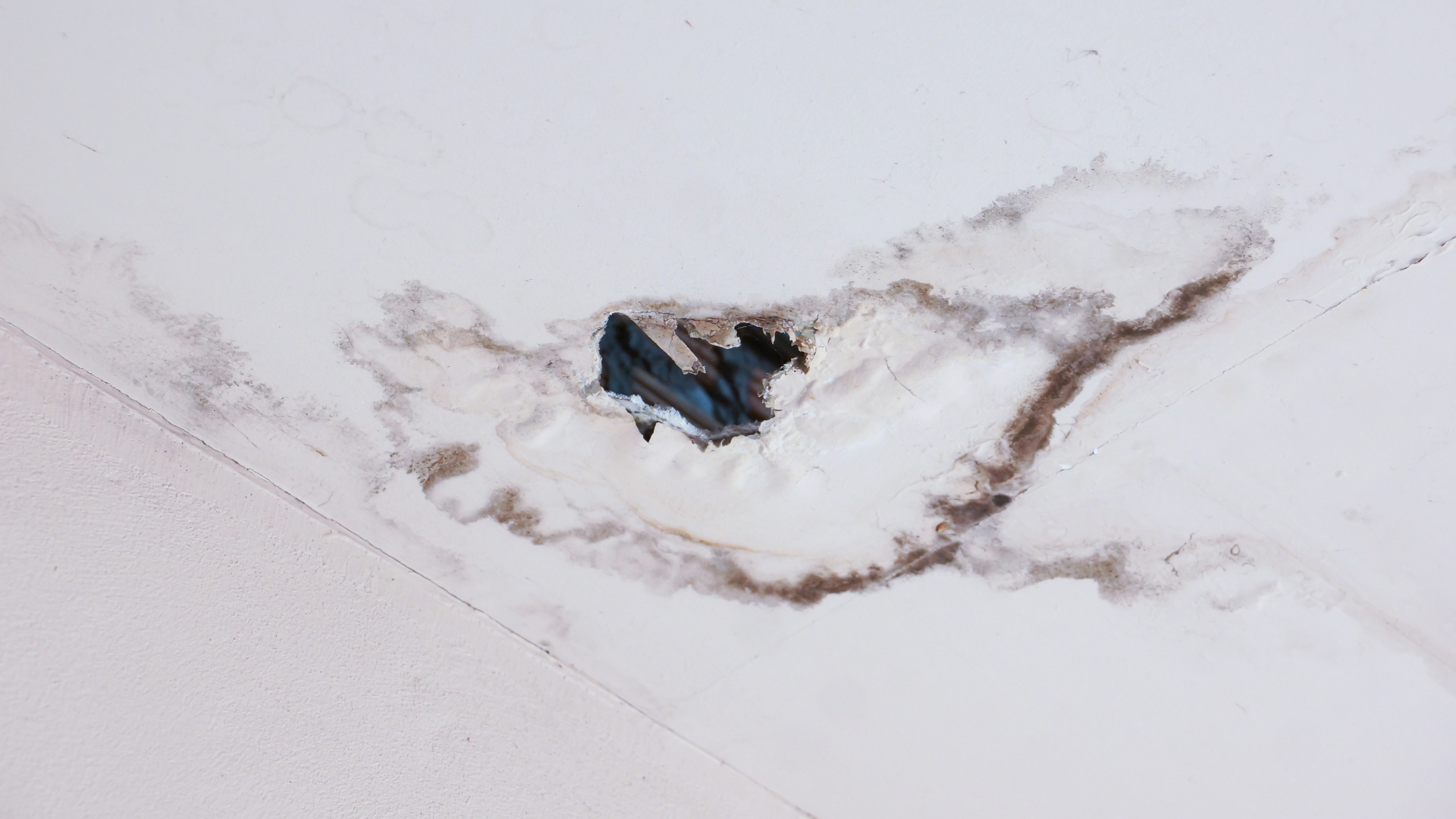 A hole in the ceiling of a building with water coming out of it.