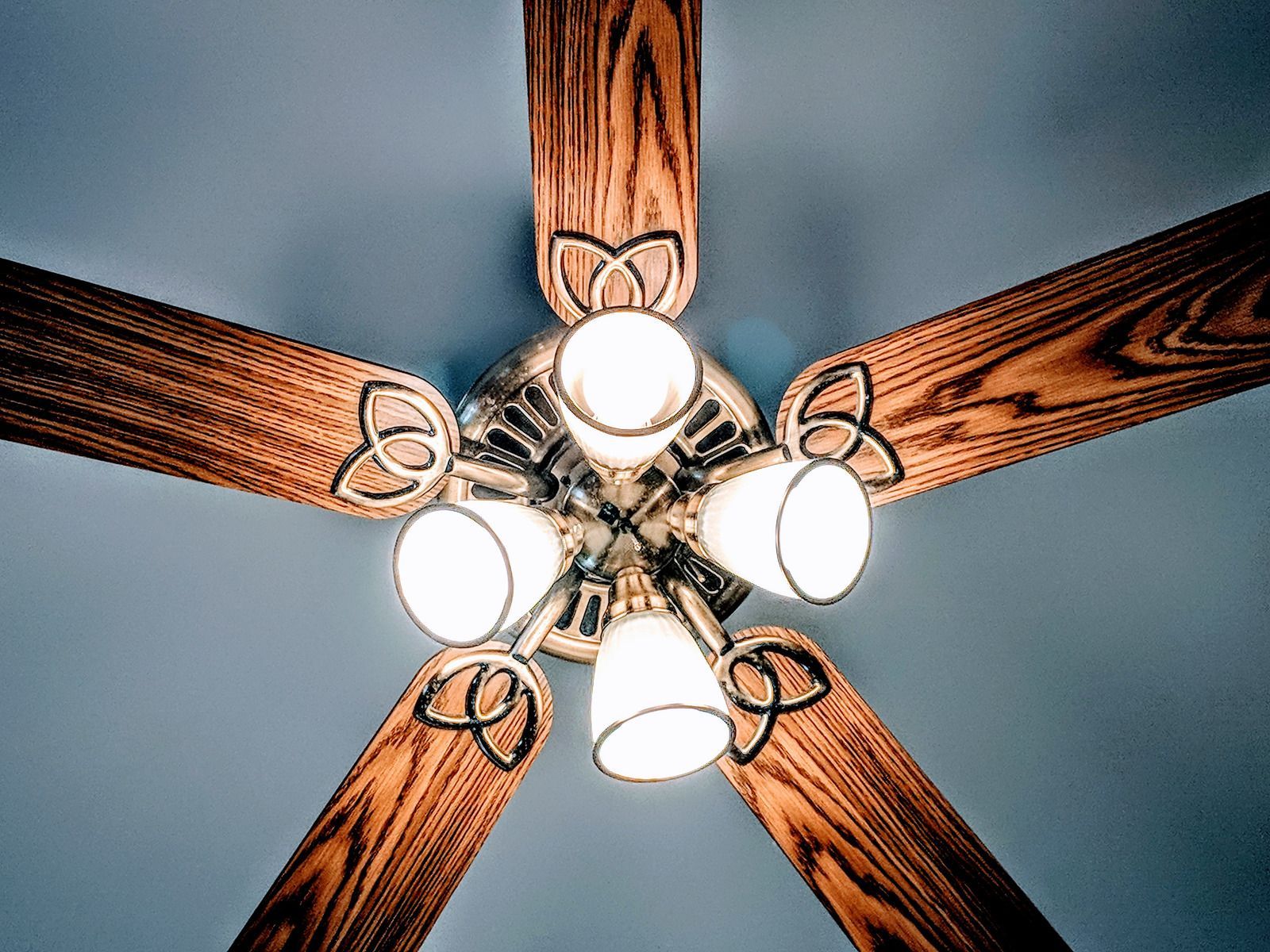 Ceiling fan with five wood-toned blades and five lights, mounted on a blue ceiling.