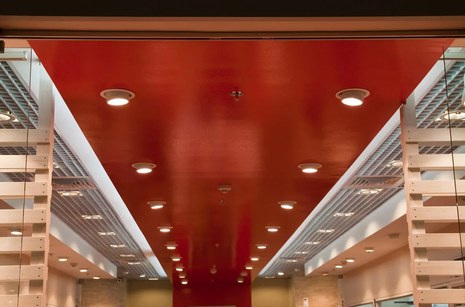 Red ceiling with recessed lights, leading into a commercial space, framed by wooden elements.