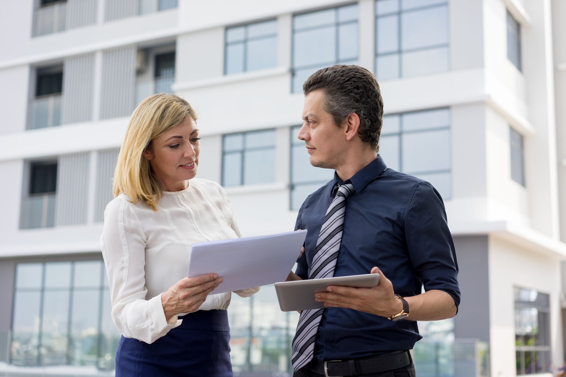 Two business people walking outside a modern office building with glass and wood panels
